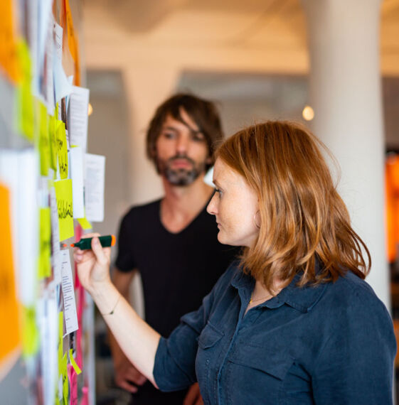 Zwei Personen arbeiten während eines Workshop mit Post-Its auf ein White-Board.