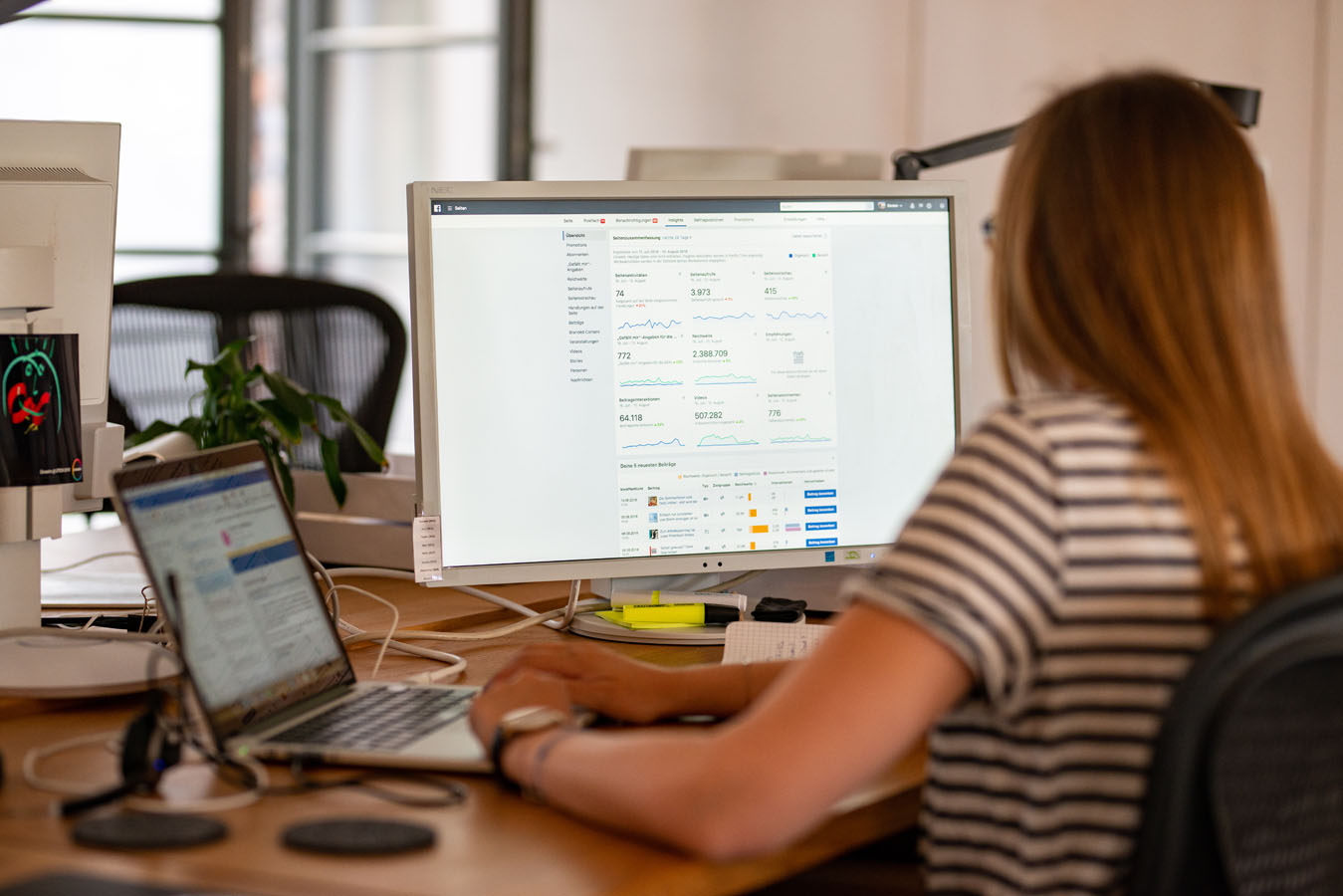 Frau sitzt am Computer und arbeitet an zwei Bildschirmen.