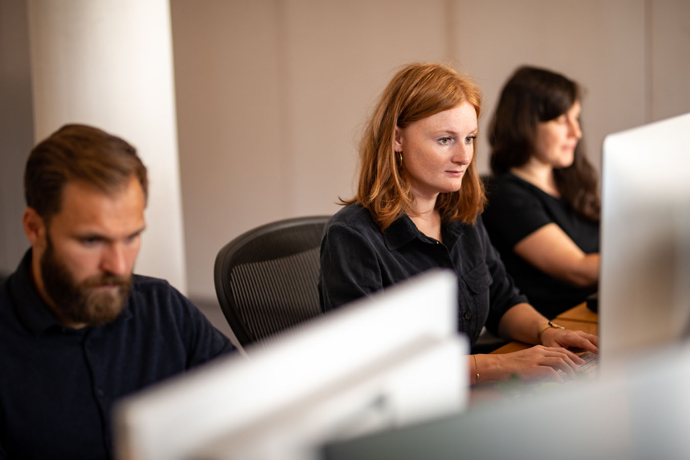 Team sitzt jeweils vor einem Bildschirm und arbeiten konzentriert.