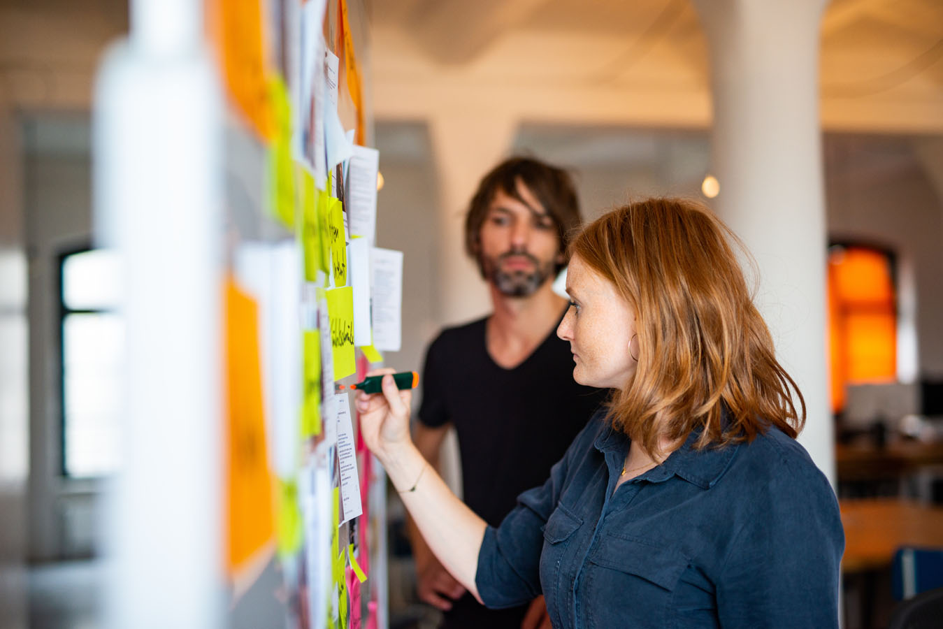 Zwei Personen arbeiten während eines Workshop mit Post-Its auf ein White-Board.